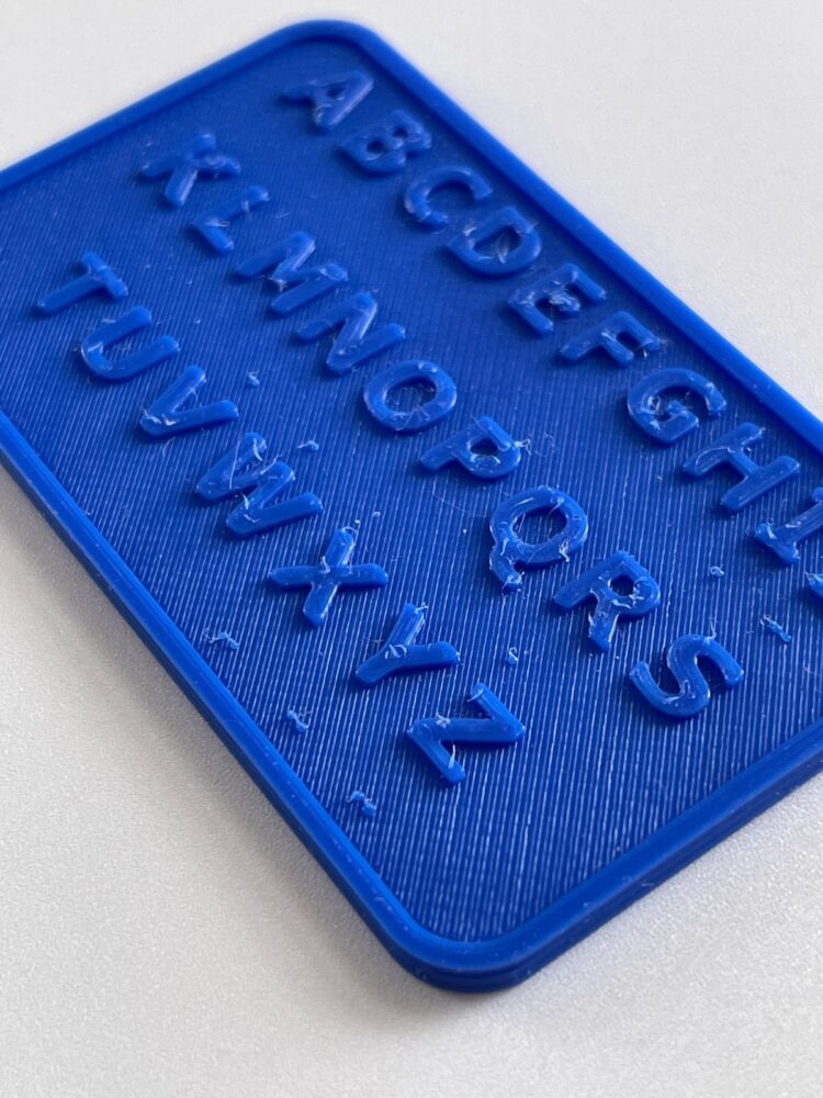 Close up image of the first attempt at 3D printing a Deaf Blind Pocket Communicator. The card has an alphabet with braille below it, but the braille has mostly been rubbed off.