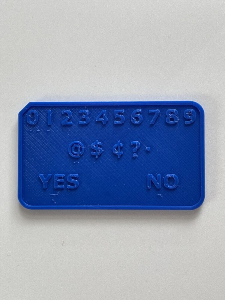 One side of the Deaf Blind Pocket Communicator with numbers, as well as an at, dollar, and cents symbols, a question mark, and a period. Yes and No are in the bottom two corners, and all text and punctuation are translated into braille that is directly beneath the text.