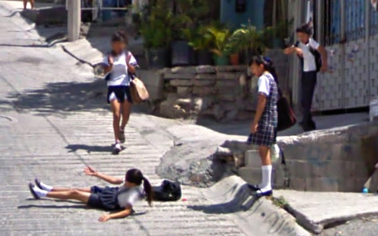 Google Maps footage of school children playing in the street and sidewalk, one laying in the street.