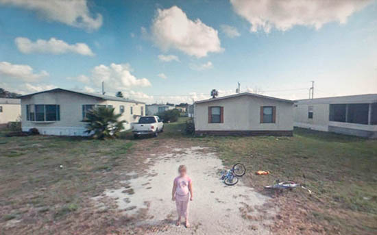 A young girl standing in the backyard of a small home. 