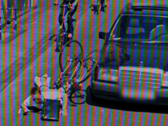Grainy image of a man falling off a bike in a street.