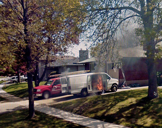 A white van on fire, parked in a residential driveway. 
