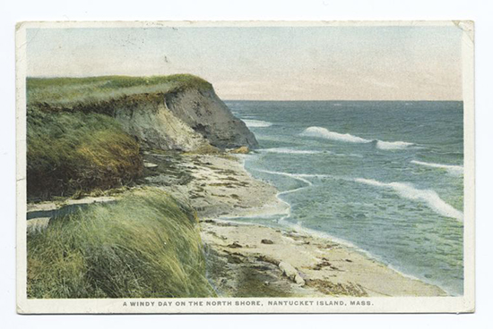 An image of a beach, grassy bluff, beige sand, and low blue waves.