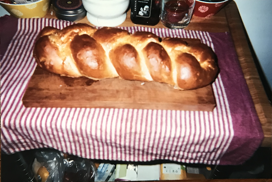 A freshly baked challah on a cutting board atop a striped red and white kitchen towel.
