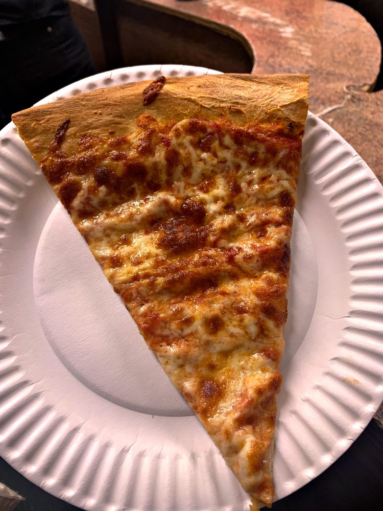 Photograph of a slice of plain pizza on a paper plate