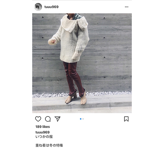 Screenshot of an Instagram post, showing a person from the neck down wearing a cardigan and brown jeans, posing against a grey background. 