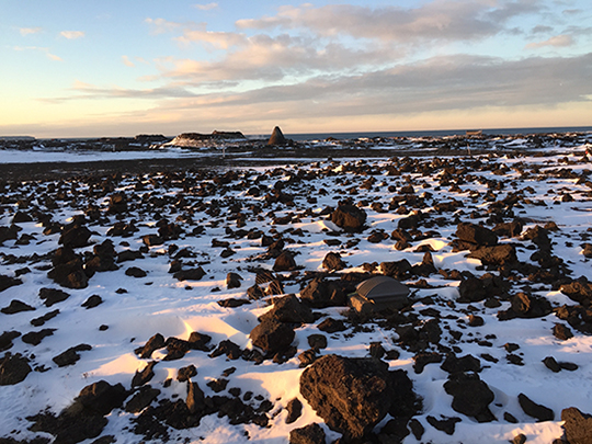 Rocky, flat expanse, partially covered in snow, under a pale and cloudy sky