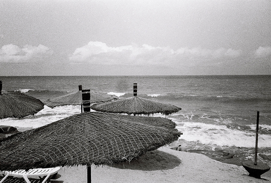 A view of the beach, with a few umbrellas set up and mild waves. 