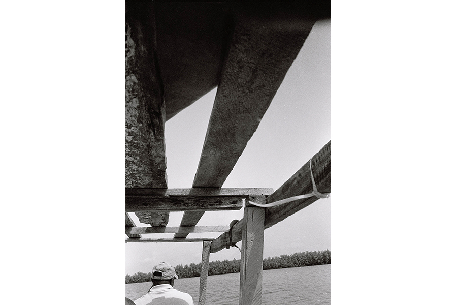 black & white photograph from boat, depicting boats framing, water and shore in background