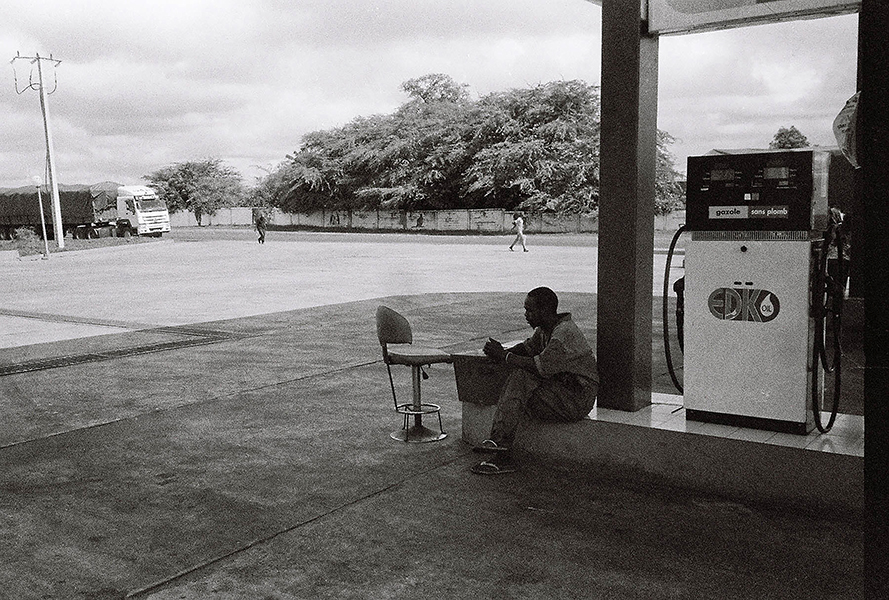 black and white photograph of person seated at edge of gas station