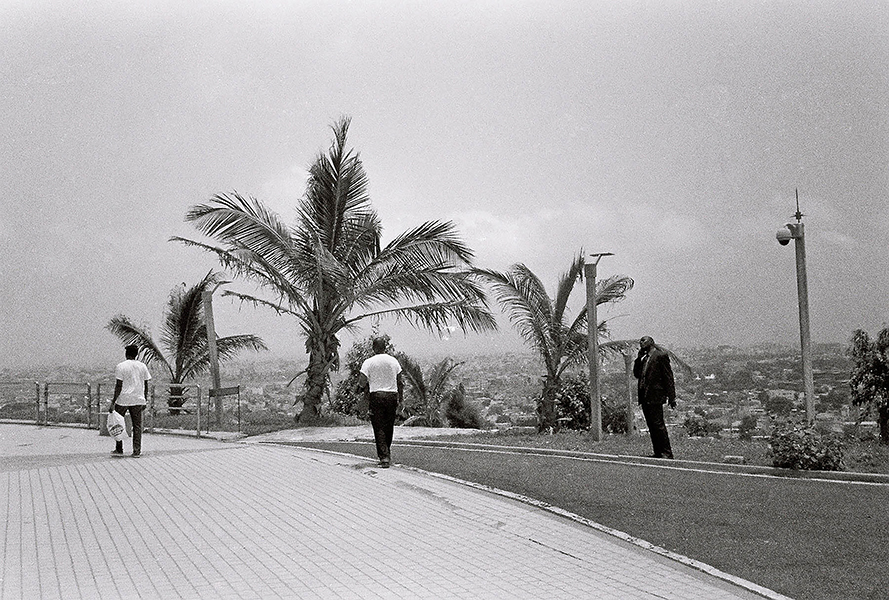 Black and white photo of a street, with large palm trees and three men walking. 