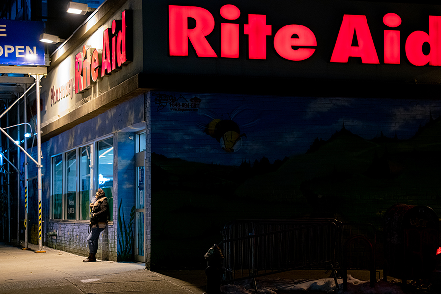 Woman smokes while leaning on the outside of a Rite Aid pharmacy. 