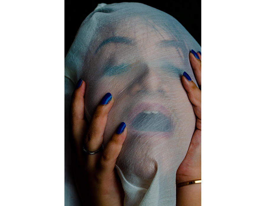 An unidentifiable woman, mouth gaping, is suffocated by a soft white fabric wrapped around the whole of her face. her hands with blue painted nails are delicately placed on either side of her face, as if longing for the air that won't seep in.