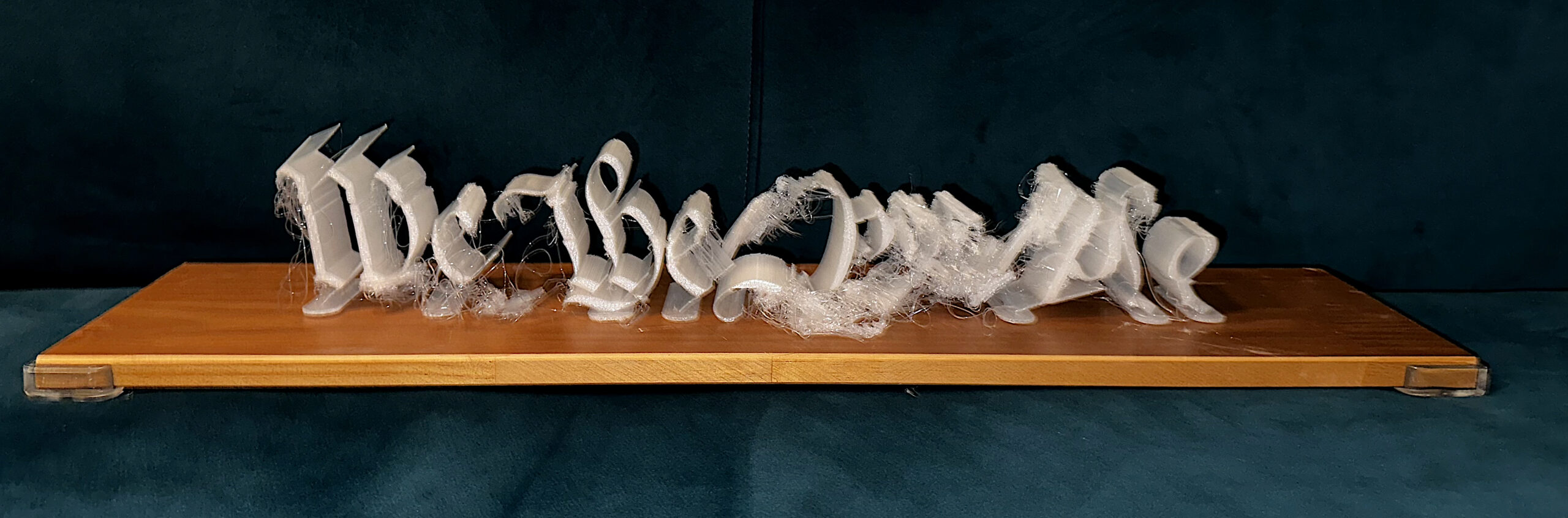 (Same alt text caption for all 3 of these) “We the People,” vertically 3D printed in transparent PLA without supports and formally assembled on a wooden stand. Each letter was printed on its own and every iteration of the artwork would produce slightly different printing errors. When the phrase is assembled, the reference to Jefferson’s handwriting on the Constitution of the United States becomes clear and the artwork stands on its own.