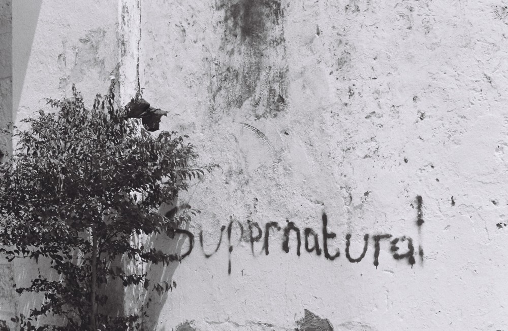 Graffiti of "supernatural" on a white wall. 