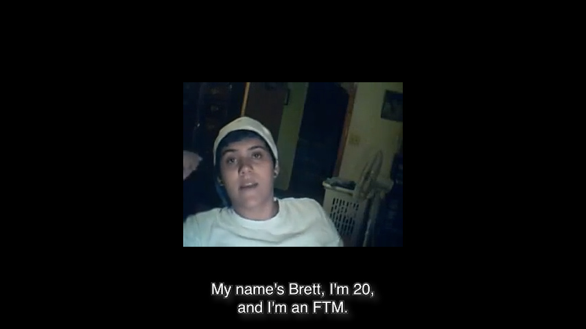 Webcam still image of a boy facing the camera. Subtitles: “My name’s Brett, I’m 20, and I’m an FTM.”