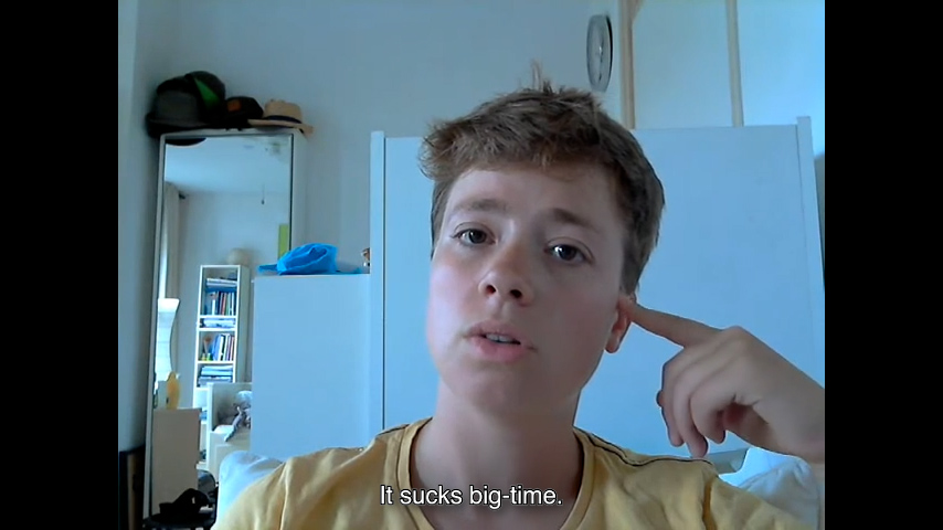 Webcam still image of a boy facing the camera. Subtitles: “It sucks big-time.”

